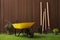 Wheelbarrow, gardening tools and plants on green grass near wood slat wall