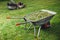 Wheelbarrow with grass and lawnmower on green lawn