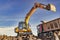 A wheeled excavator loads a dump truck with soil and sand. An excavator with a high-raised bucket against a cloudy sky View from