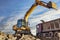 A wheeled excavator loads a dump truck with soil and sand. An excavator with a high-raised bucket against a cloudy sky View from