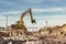 A wheeled excavator in a trench digs the ground. An excavator with a highly raised bucket against a cloudy sky. Earthworks at the