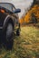 Wheels of an SUV on wet, fading grass at the edge of a forest in the Russian outback on a cloudy autumn day