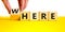 Where or here symbol. Businessman turns a wooden cube, changes the word `where` to `here`. Beautiful yellow table, white