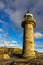 Whitby harbour lighthouse in sumer with blue sky and golden sun