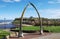 Whitby, UK. An archway made of whale bones seen on a sunny day under a blue sky. Whitby Abbey is visible through the arch.