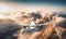 White airplane flying above mountains and low clouds at sunset