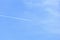 White airplane trail in a bright blue sky. The plane, leaving a trail, flies in the spacious clean bright blue skie