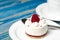 White airy cake with raspberry layer and raspberry berry lies on a white round plate next to a white cup, which stands on a blue
