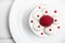 White airy cake with raspberry layer and raspberry berry lies on a white round plate next to a white cup, which stands on a white