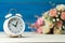 White alarm clock and flowers pink and red rose on wooden table and blue background with copy space for add text and content