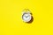 White alarm clock with hard shadow on yellow background. Top view. Wake up alert concept. Morning routine