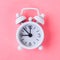 White alarm clock on a pastel blue, pink background.