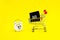 A white alarm clock, a shopping cart, and a black square that says black Friday on a yellow background. The topic of sales