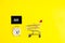 A white alarm clock, a shopping cart, and a black square that says black Friday on a yellow background. The topic of sales