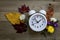 White alarm clock surounded by fresh fall flowers foliage on wooden board flat lay copy space