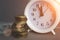 White alarmclock with Coins stack and stack of one hundred dollar bills on grey background. Deadline and time is money concept,