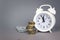 White alarmclock with Coins stack and stack of one hundred dollar bills on grey background. Deadline and time is money concept