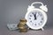 White alarmclock with Coins stack and stack of one hundred dollar bills on grey background. Interest rate, dividend concept,