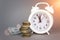 White alarmclock with Coins stack and stack of one hundred dollar bills on grey background. Save money for prepare in the future.