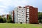 White apartment building with red building block sidewalls and multiple balconies surrounded with grass and tall trees