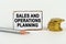 On a white background, a pencil, coins and a sign with the inscription - Sales and Operations Planning