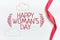 On a white background, a red ribbon with a row of abstract inscription - Happy Women`s Day with branches on the sides and clouds.