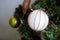 A white ball wrapped in a waxed cord hangs on an artificial Christmas tree decorated in rustic style