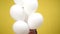 White balloons with charming teenage Caucasian girl emerging at yellow background smiling. Positive beautiful slim