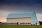 White barn at sunset in a green, grassy field under a sky with purple, yellow, and orange clouds