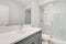 A white bathroom with a grey vanity and white tiled shower.