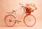 A white bicycle with a basket full of flowers, on peach fuzz background.