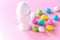 White big egg in the stand and small colorful candy eggs. Easter celebrate concept. Pink background