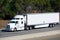 White big rig long haul semi truck transporting commercial cargo in refrigerator semi truck