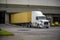 White big rig professional semi truck with container trailer unloading cargo standing in warehouse dock with gates