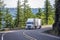 White big rig semi truck transporting goods in refrigerated semi trailer turning on the mountain road with rock wall