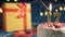 White birthday cake number 17 golden candles burning by lighter, blue background with lights and gift yellow box tied up with red