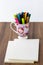 White blank books on wooden background with a teacup filled with colorful brush pens