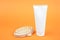 White blank cosmetic tube of cream or body lotion and wooden anti-cellulite massager on orange background. Concept fight against