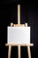 White blank cotton canvas stands on a wooden artistic easel on black curtain background. Horizontal rectangular mockup canvas
