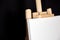 White blank cotton canvas stands on a wooden artistic easel on black curtain background. Horizontal rectangular mockup canvas