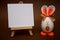 White blank paper on easel with funny egg in form of cute bunny on brown background