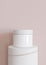 White and blank, unbranded cosmetic cream jar with flying golden ring on pink background. Skin care product presentation