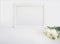 White blank wooden frame mockup with the Persian buttercup and daffodil flowers lying on the white table. Poster product design. S