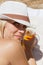 White blonde girl in a white hat sunbathes on the beach, smiling and holding a glass of cold beer, quenching of thirst