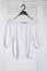 White blouse hanging on a hanger. White wooden screen on the background. Fashionable wardrobe