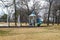 A white and blue jungle gym and a swing set in the park surrounded by yellow winter grass and bare winter trees