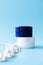 White and blue moisturizer cream jars and small minerals on blue background, front view. Mockup cosmetic branding