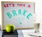 A white board titled `Let`s take a brake` with red and green letters, cup of milk and a green apple.