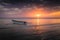 White boat on the sea with an orange-purple sunset sky reflected in the water, Zanzibar, Tanzania