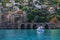 White boat in turquoise water against the background of an ancient stone wall with arched gates and modern cottages on a hillside